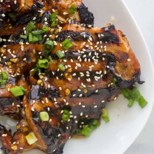 Teriyaki chicken thighs lined up on a serving platter beside a striped dishtowel