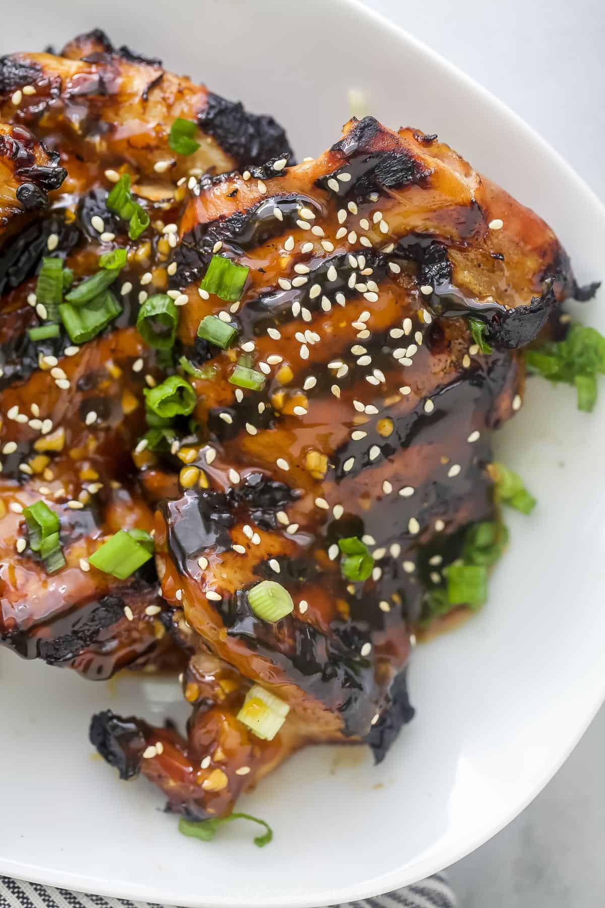 Two teriyaki grilled chicken thighs topped with sesame seeds and chopped green onion