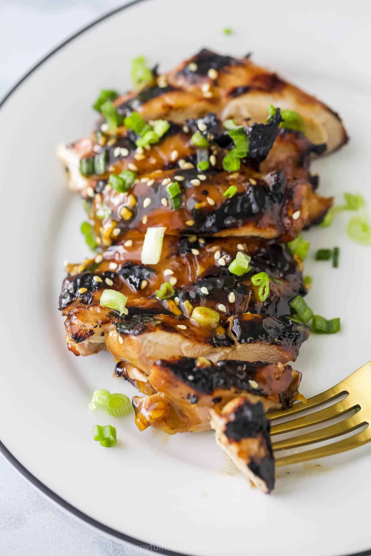 A plate of sliced teriyaki grilled chicken with a fork picking up a small piece