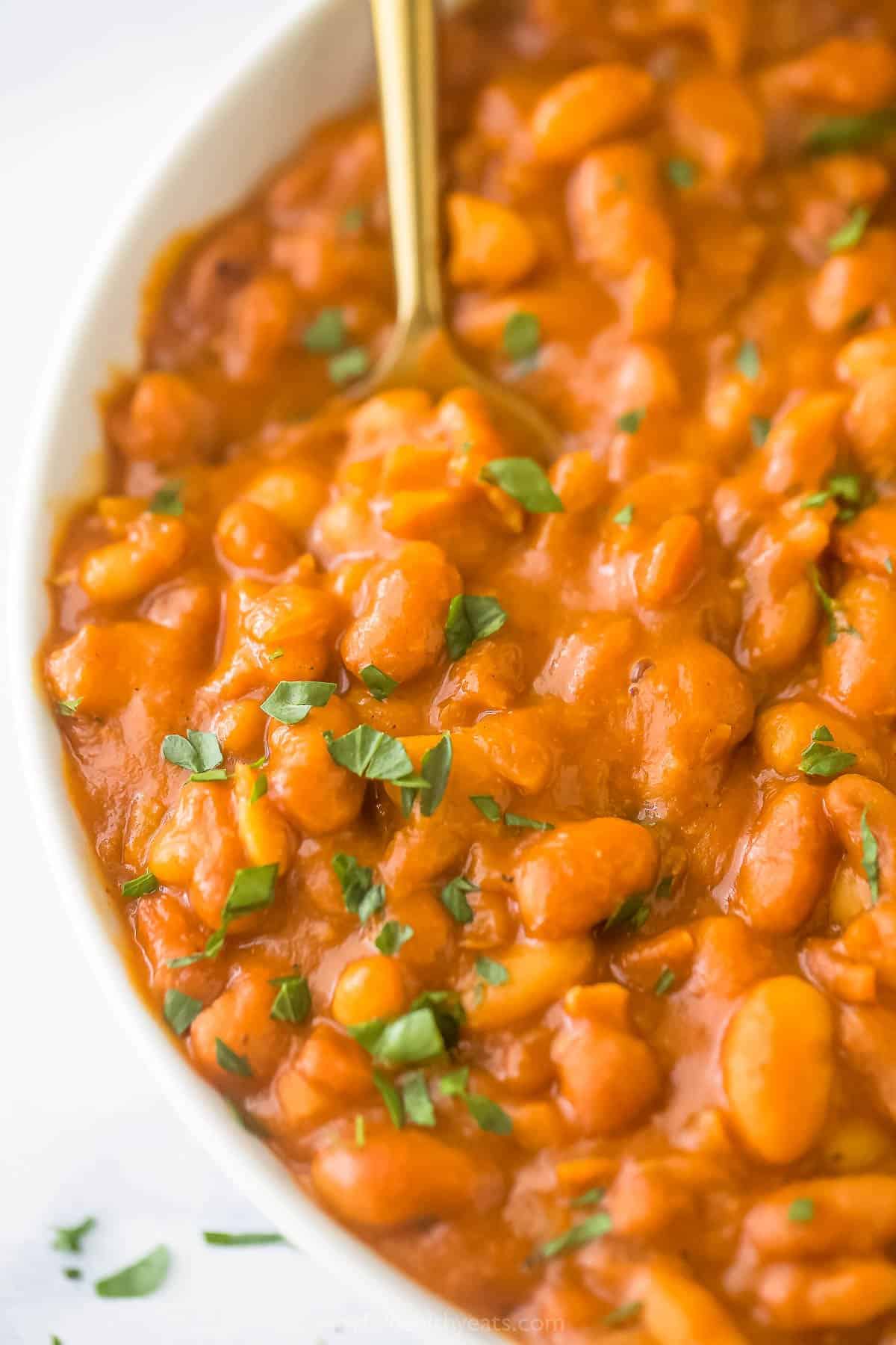 A close-up shot of homemade baked beans garnished with fresh chopped parsley