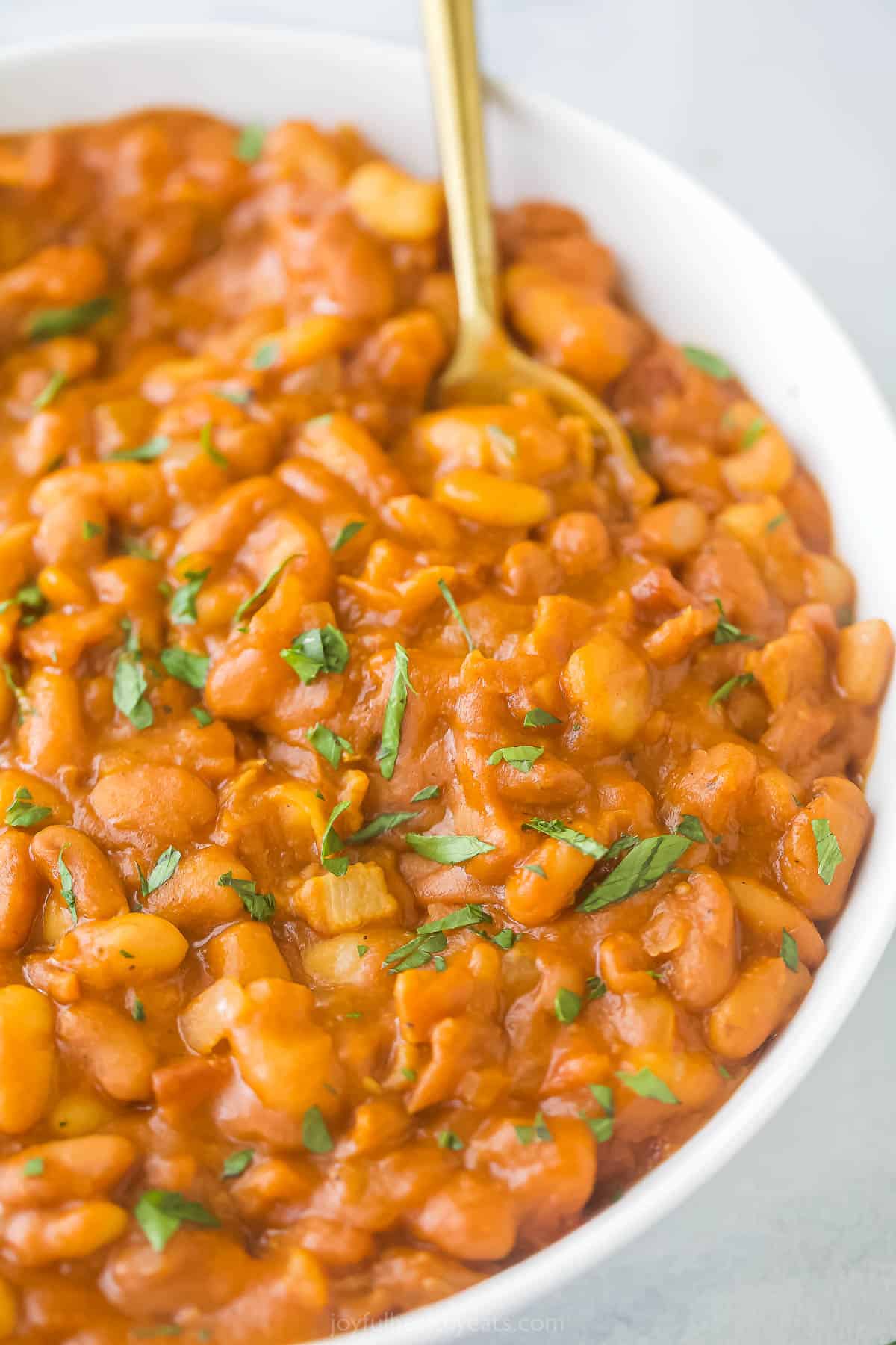 A large bowl of bacon baked beans with a golden spoon inside