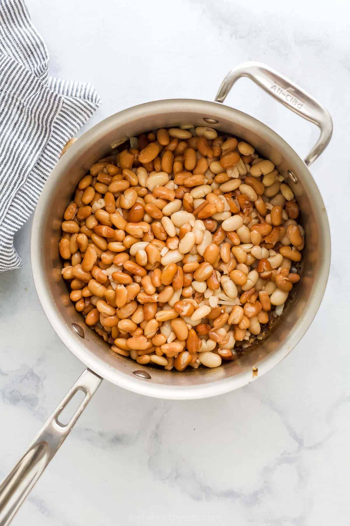 Drained and rinsed beans inside of a saucepan with sautéed bacon, onions and garlic