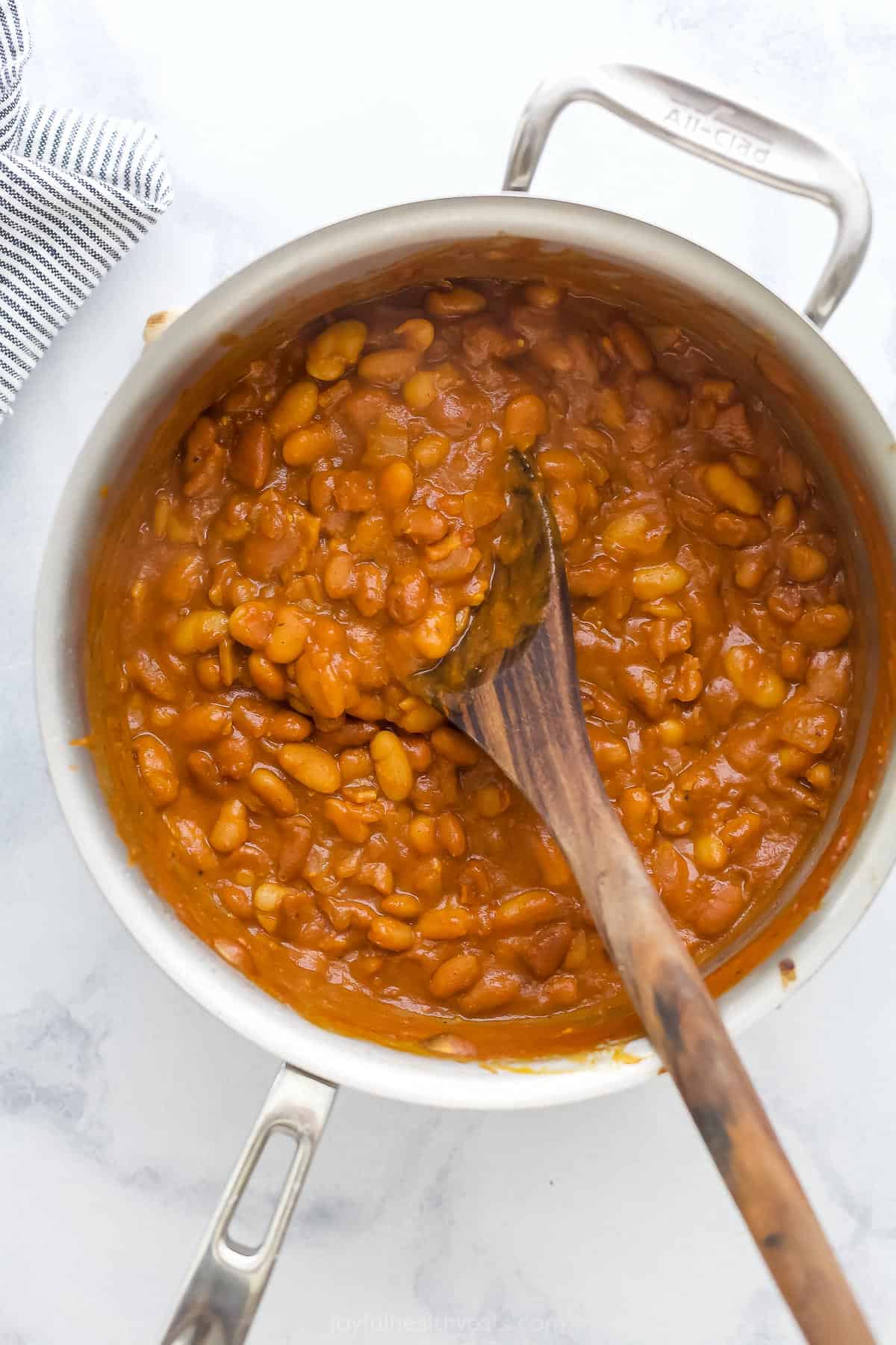 A big saucepan full of baked beans beside a striped kitchen towel