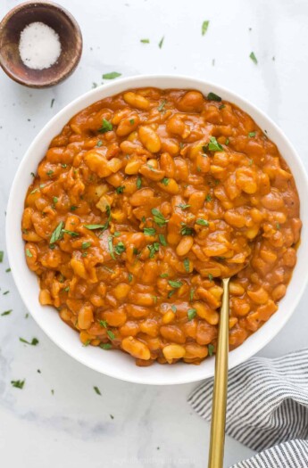 A large serving bowl full of homemade baked beans with chopped herbs on top as a garnish
