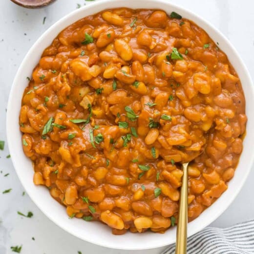 A large serving bowl full of homemade baked beans with chopped herbs on top as a garnish