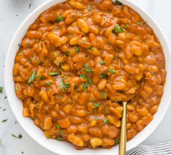 A large serving bowl full of homemade baked beans with chopped herbs on top as a garnish