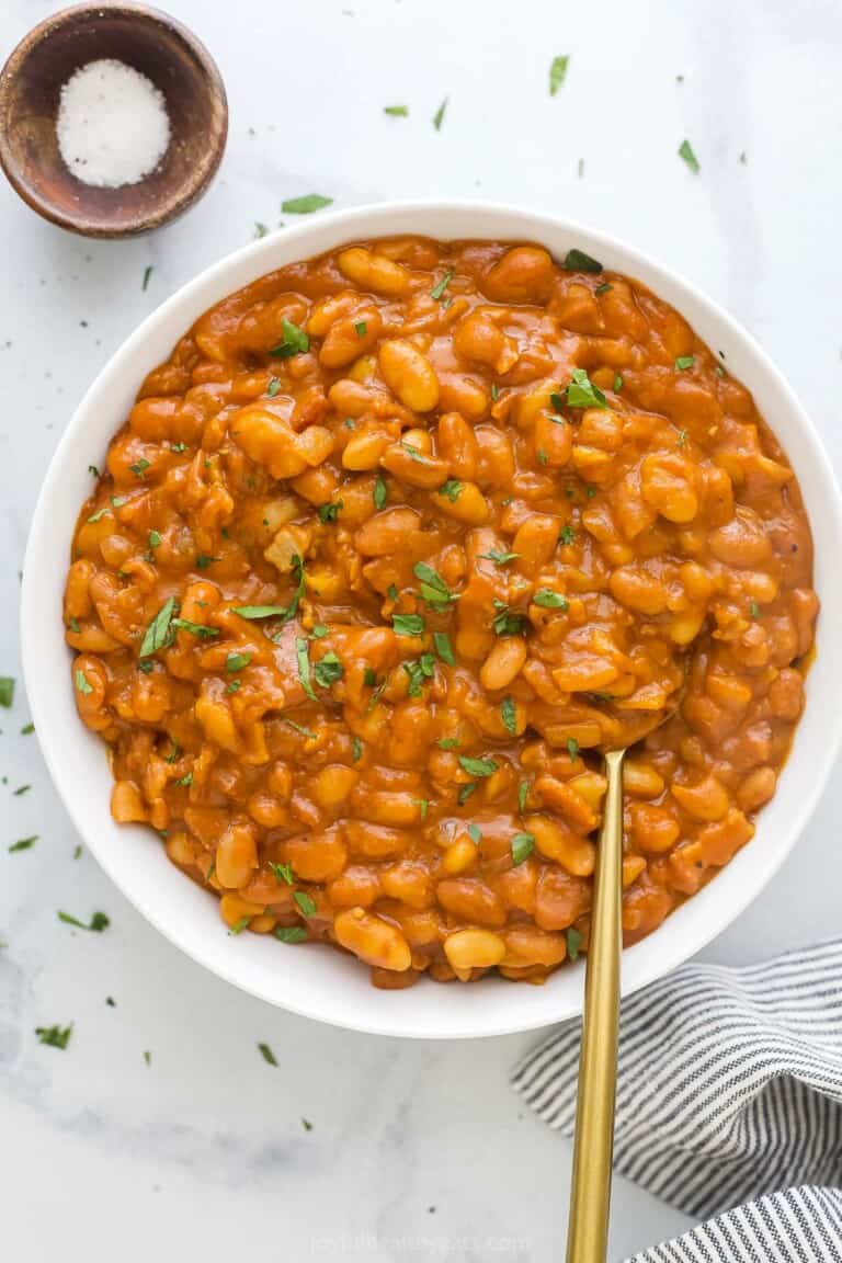 A large serving bowl full of homemade baked beans with chopped herbs on top as a garnish