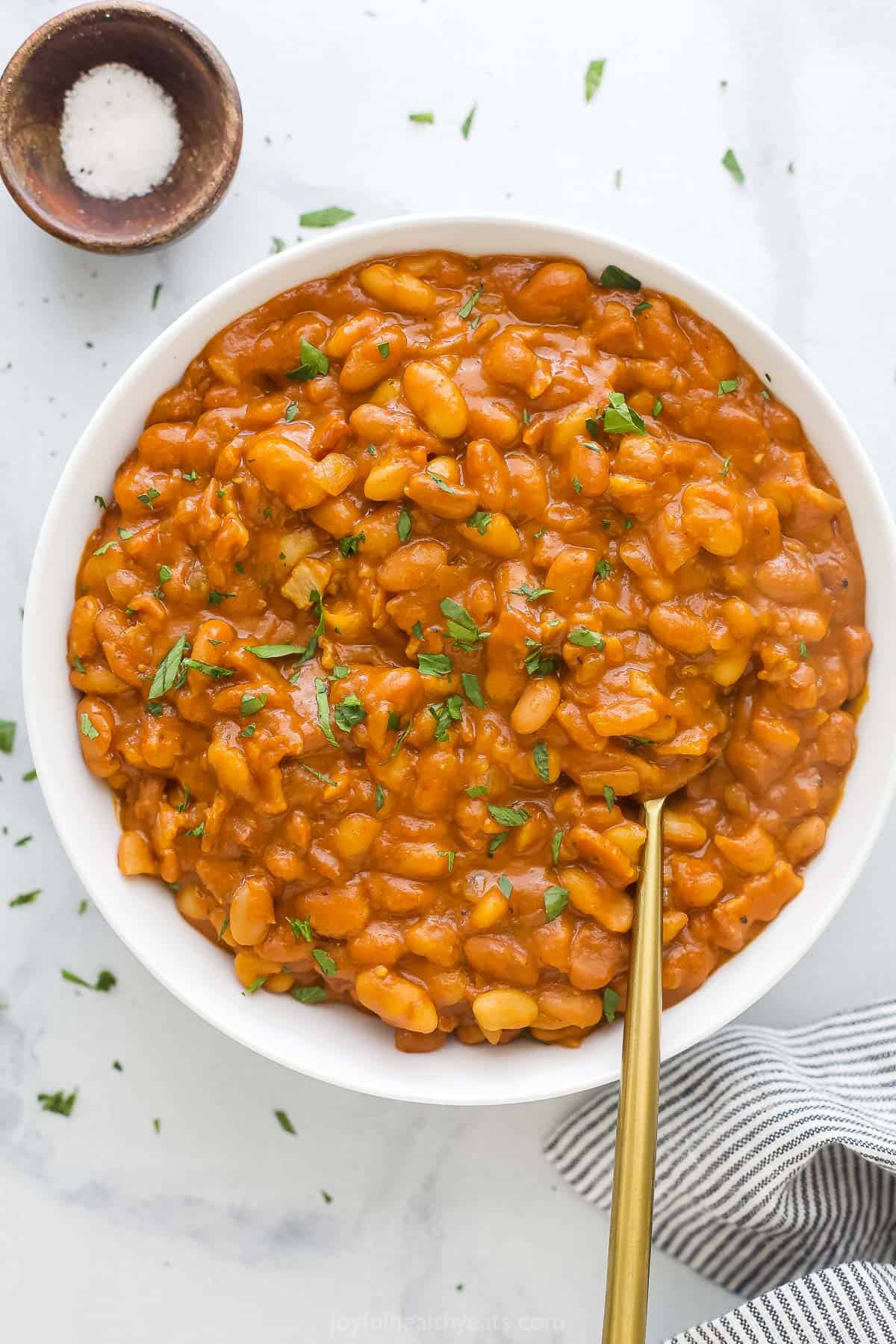 A large serving bowl full of homemade baked beans with chopped herbs on top as a garnish