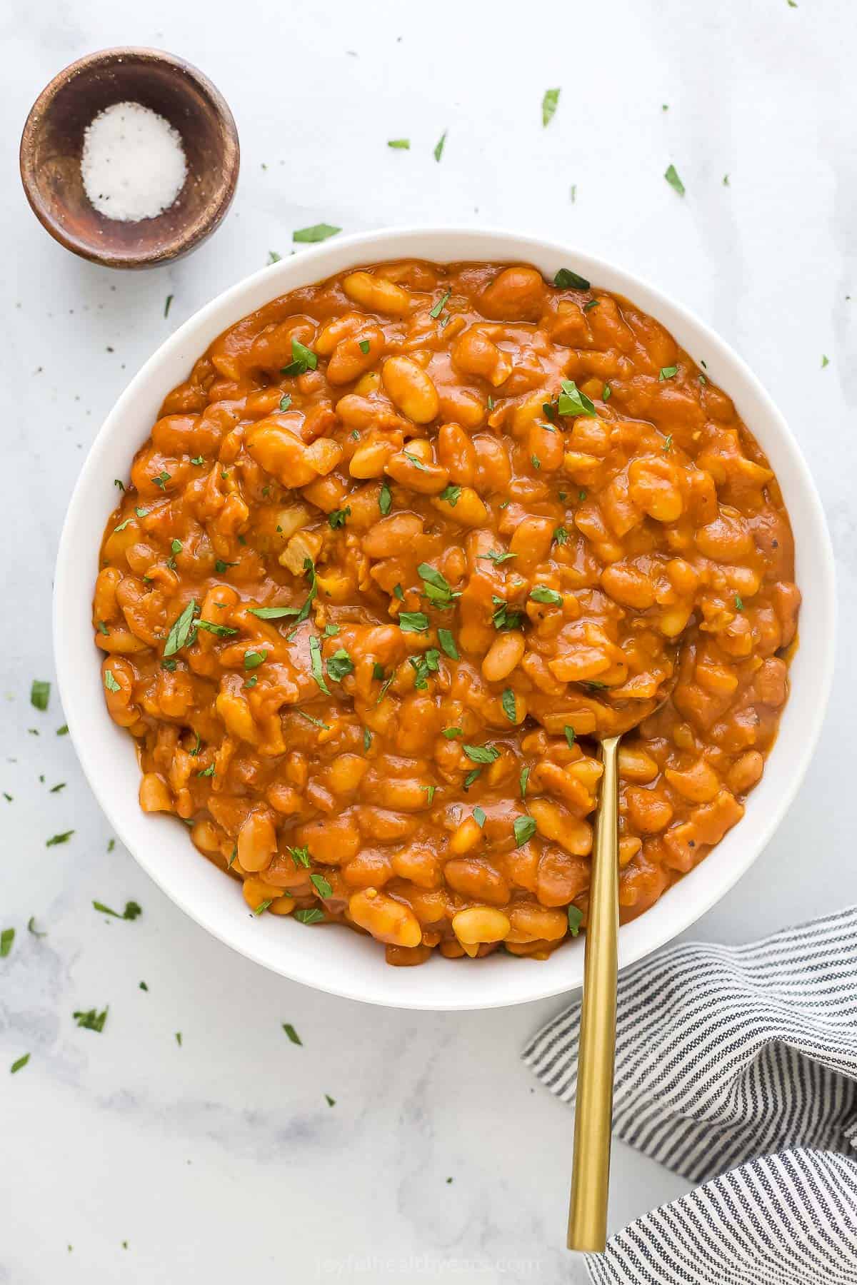 Bacon baked beans in a big bowl with chopped parsley sprinkled on top