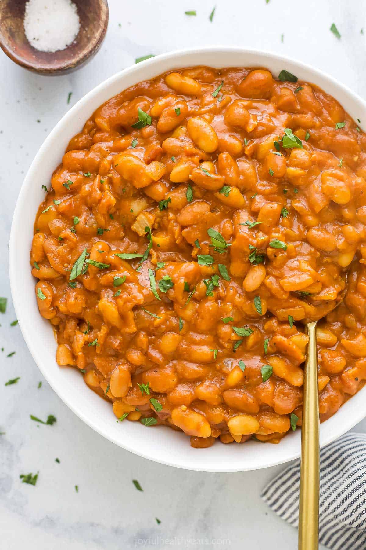 A bowl of baked beans on a kitchen countertop beside a small dish of salt