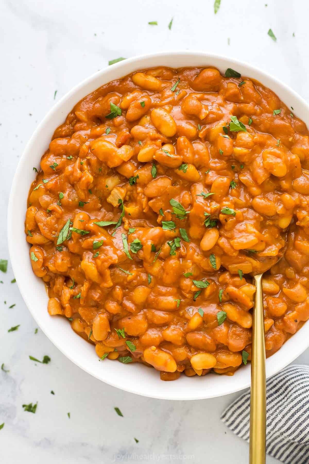 A big bowl of baked beans on a marble countertop with a striped dishtowel beside it