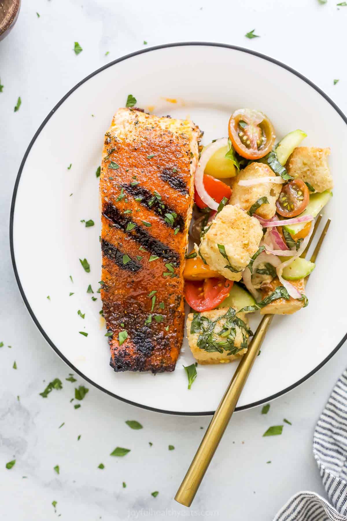 A blackened salmon fillet on a plate with a serving of salad.