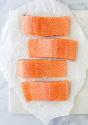 Four skin-on salmon fillets lined up on a sheet of parchment paper.