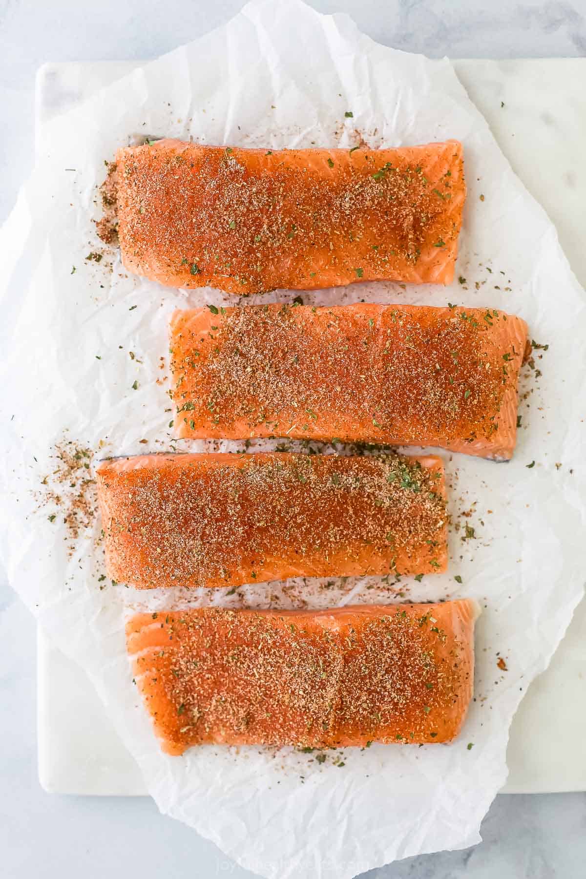 Four seasoned fish fillets on a sheet of parchment paper on top of a cutting board