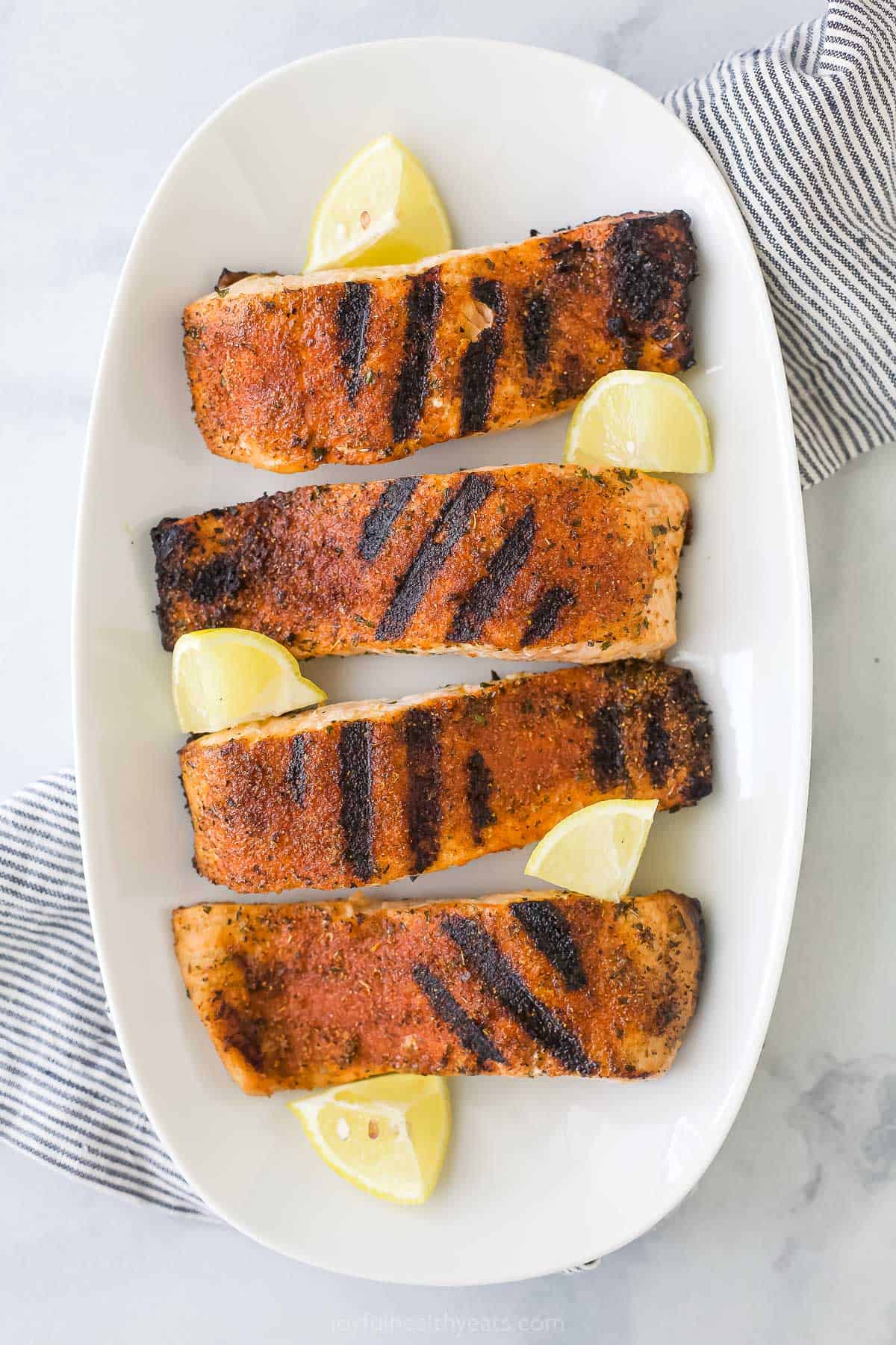 Grilled salmon fillets on a serving platter on top of a striped kitchen towel