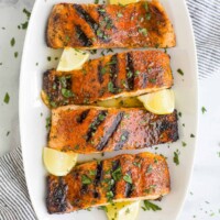 A white platter holding four blackened salmon fillets and five fresh lemon wedges