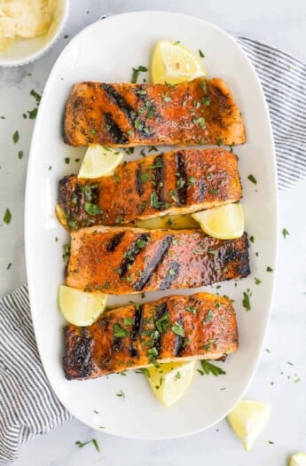 A white platter holding four blackened salmon fillets and five fresh lemon wedges