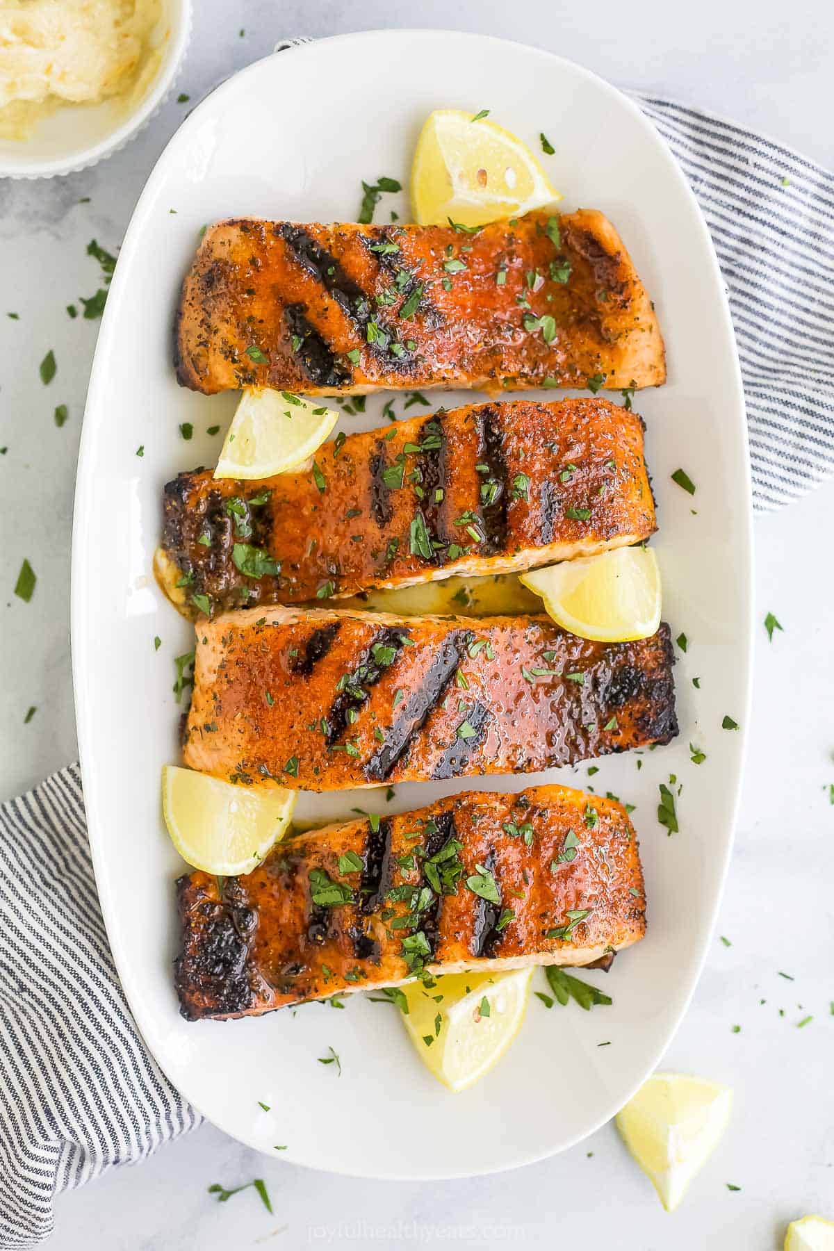 A white platter holding four blackened salmon fillets and five fresh lemon wedges.