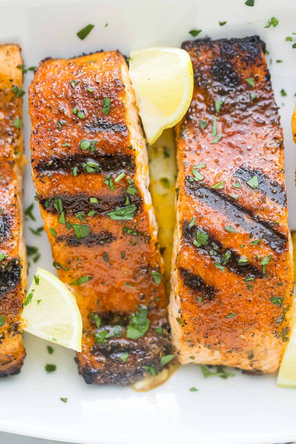 Blackened fish fillets on a plate with chopped parsley and honey butter on top.