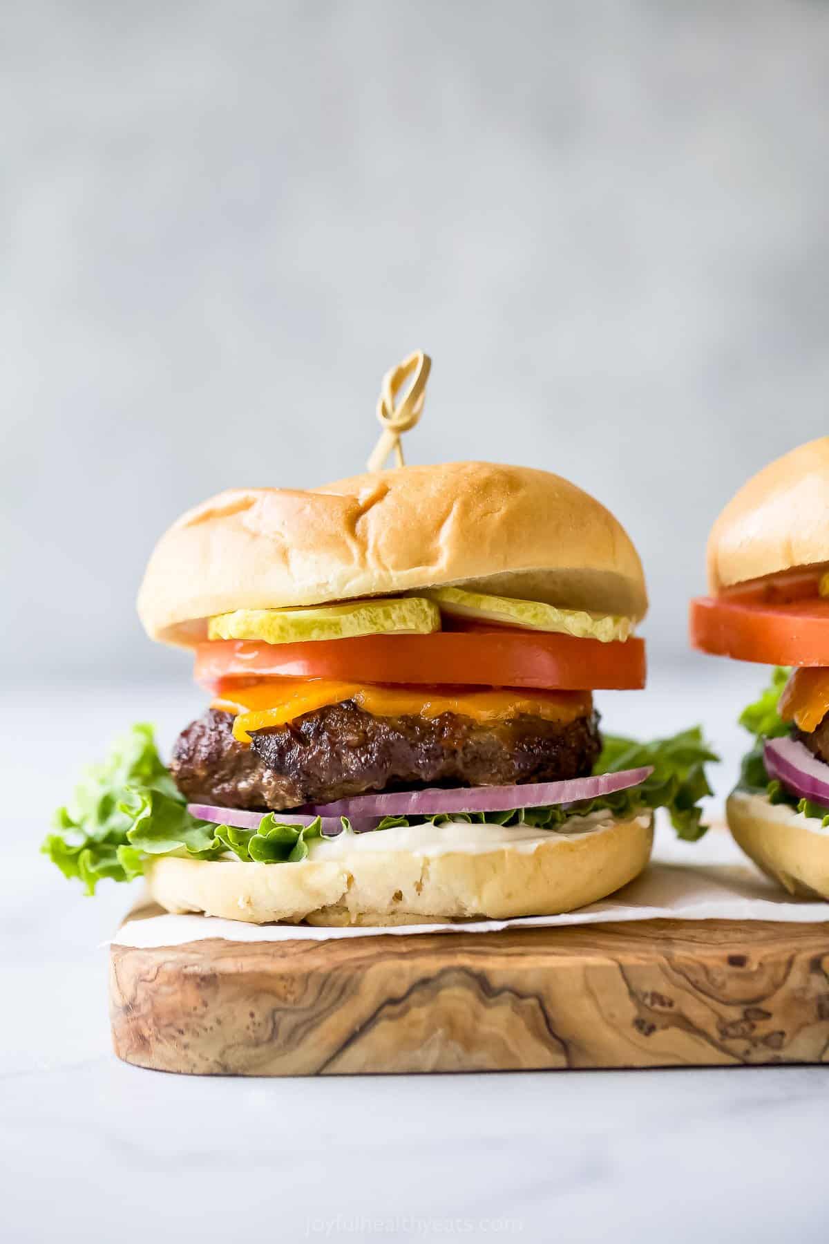 Hamburger with cheese, lettuce, tomato, red onion, and pickle on a cutting board