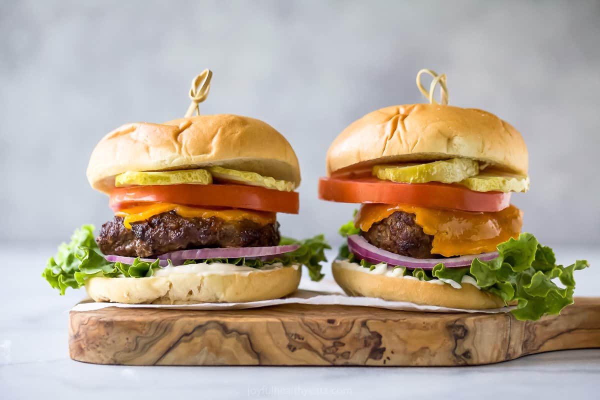 Hamburger with cheese, lettuce, tomato, and pickle on a cutting board