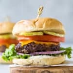 Hamburger with cheese, lettuce, tomato, and pickle on a cutting board
