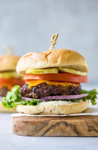 Hamburger with cheese, lettuce, tomato, and pickle on a cutting board