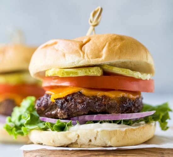 Hamburger with cheese, lettuce, tomato, and pickle on a cutting board