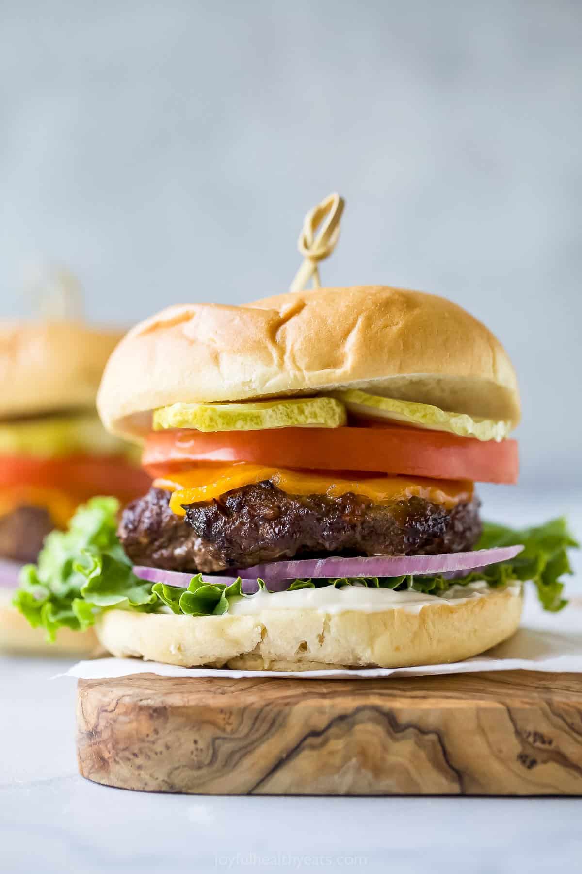 Hamburger with cheese, lettuce, tomato, onion, and pickle on a cutting board