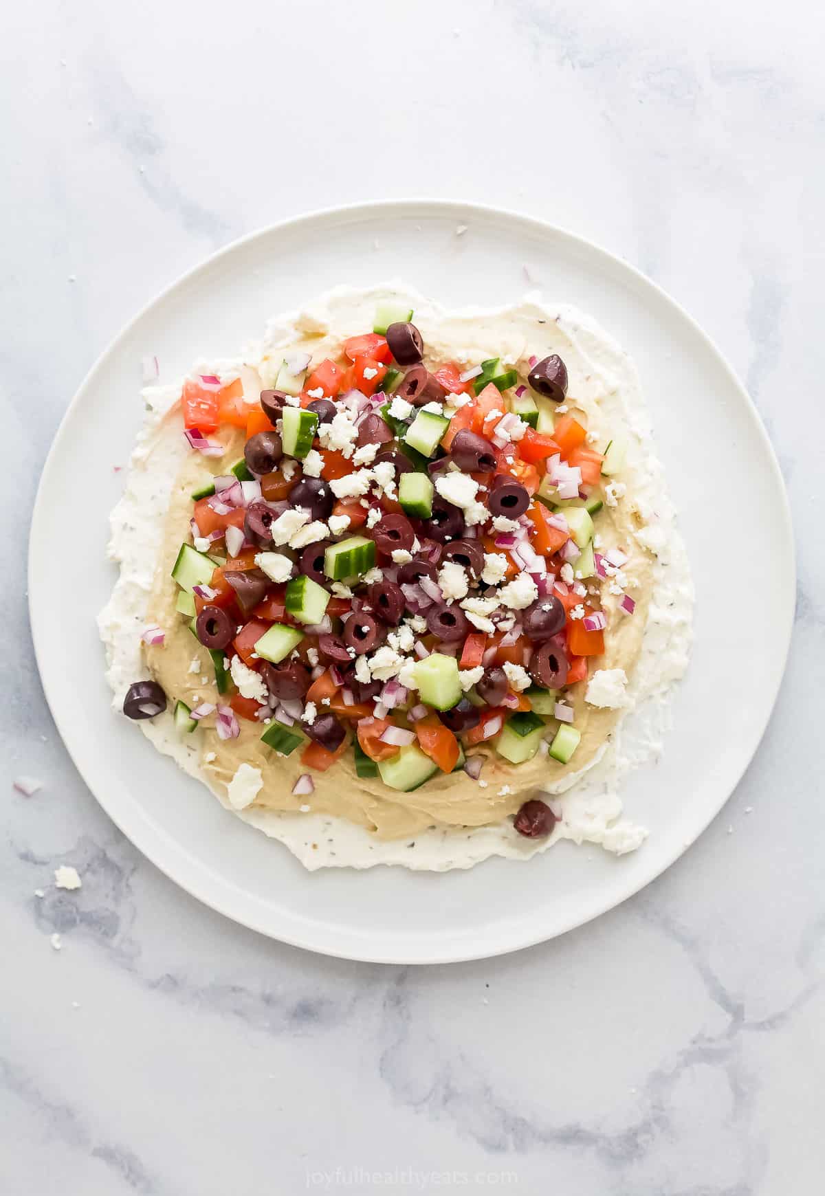 A plate full of seven layer dip on a marble kitchen countertop