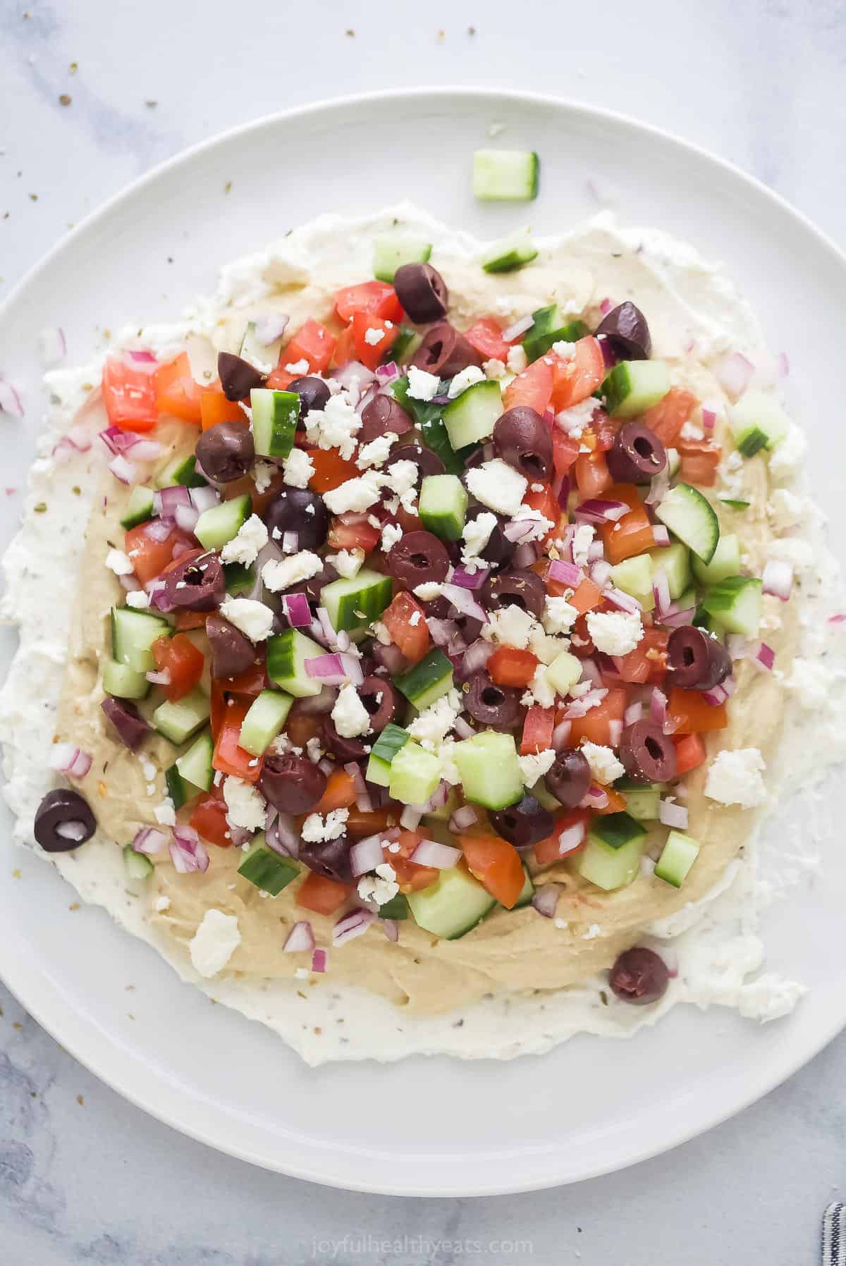 A 7 layer dip on a big plate on top of a white and gray marble surface