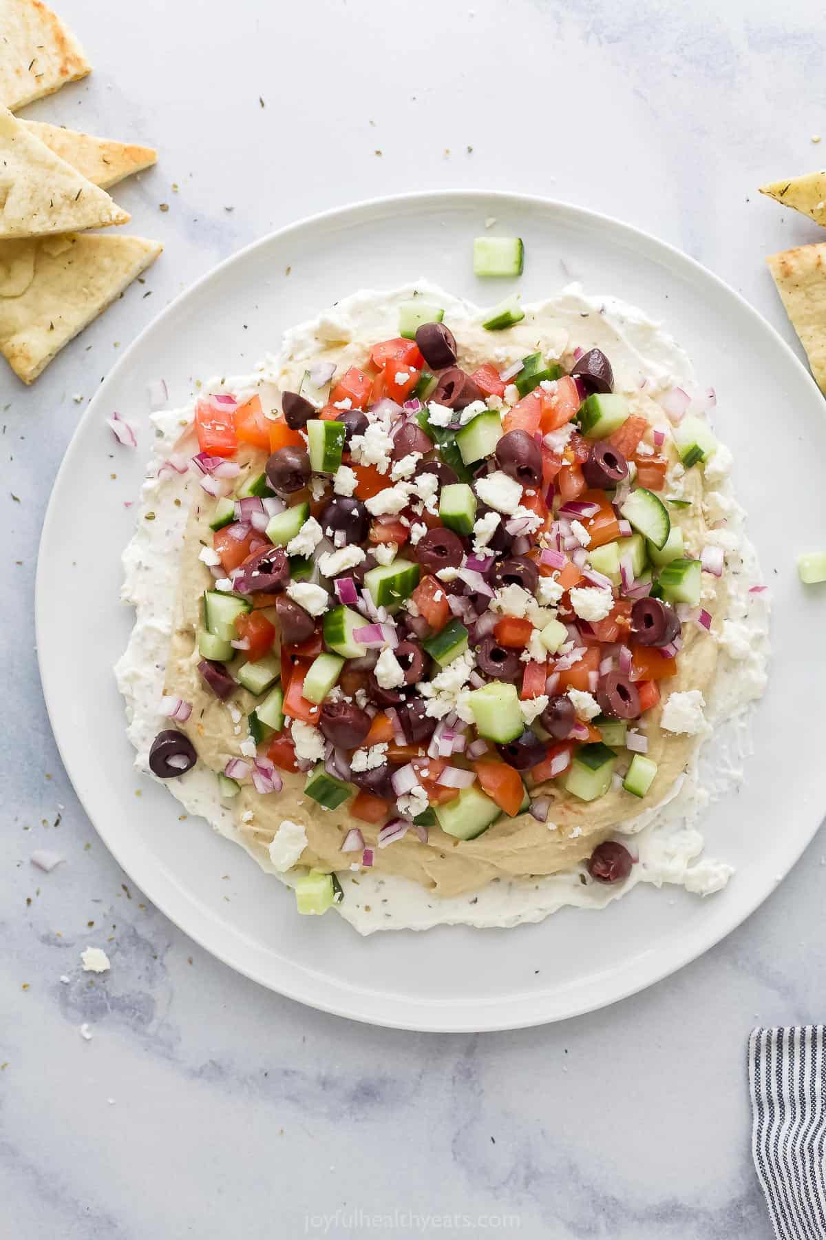 A plate of dip on a kitchen countertop with a few loose pita chips beside it