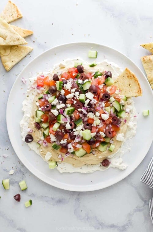 A 7 layer dip on a large plate with pita chips beside it