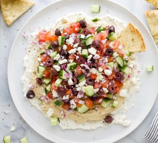 A 7 layer dip on a large plate with pita chips beside it