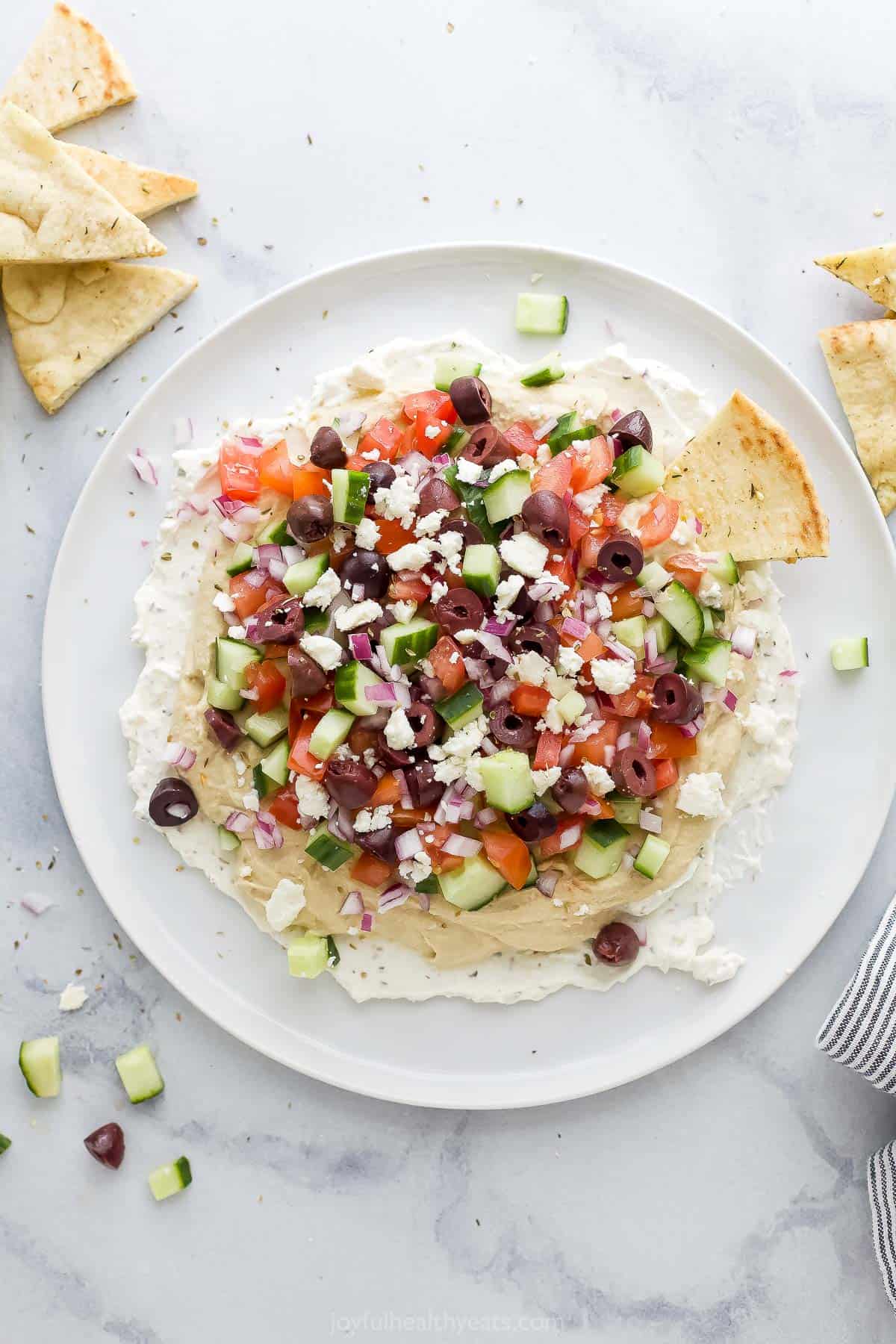 A 7 layer dip on a large plate with pita chips beside it