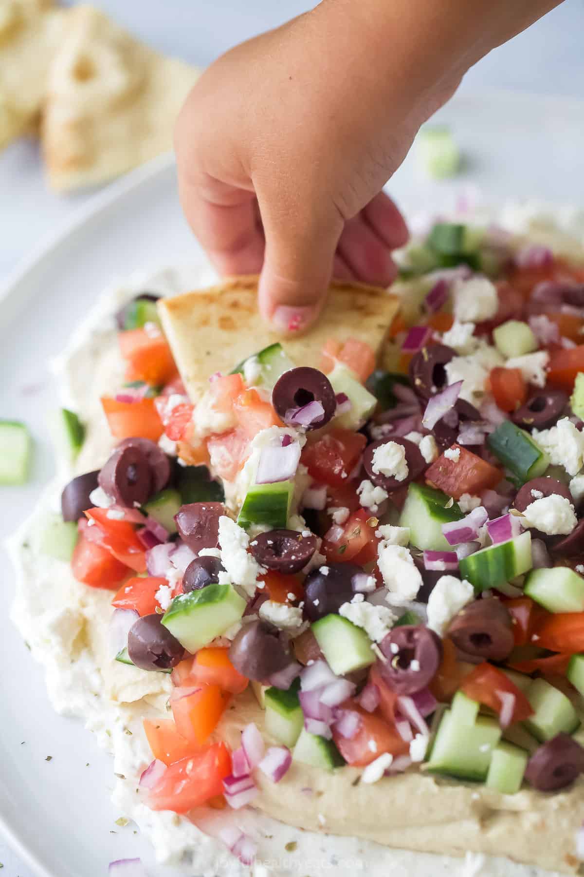 A hand dipping a baked pita chip into a 7 layer dip on a serving plate