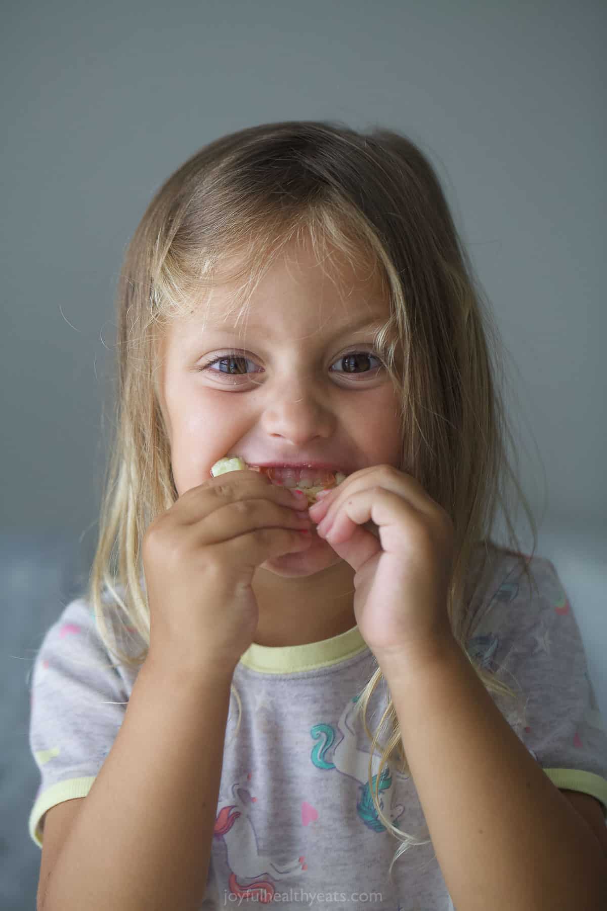 Krista's daughter eating a dip-filled pita chip with a smile on her face