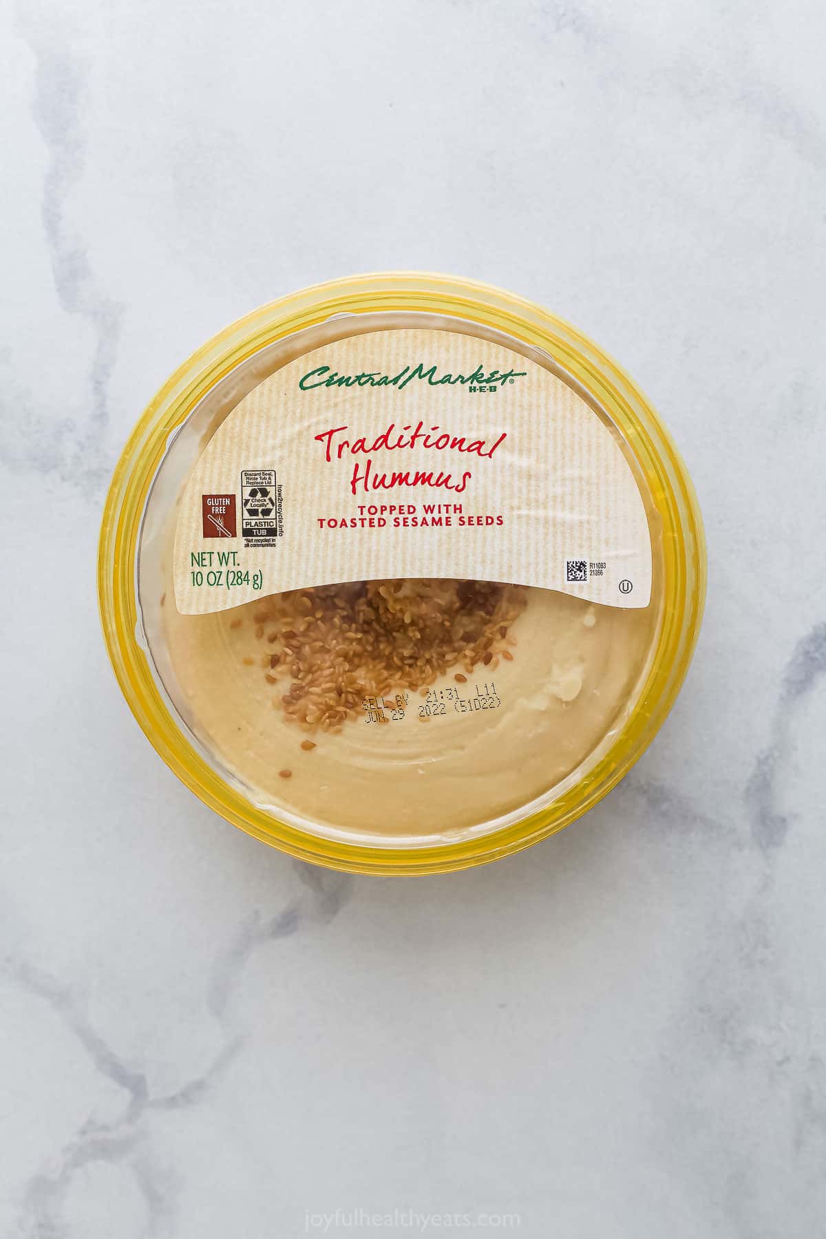A tub of store-bought hummus sitting on a white and gray marble surface