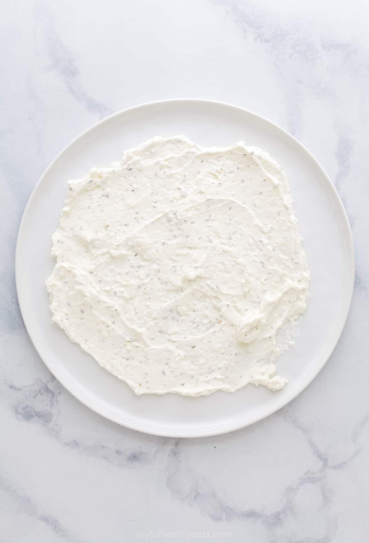 Whipped feta spread onto a large white plate in an even layer