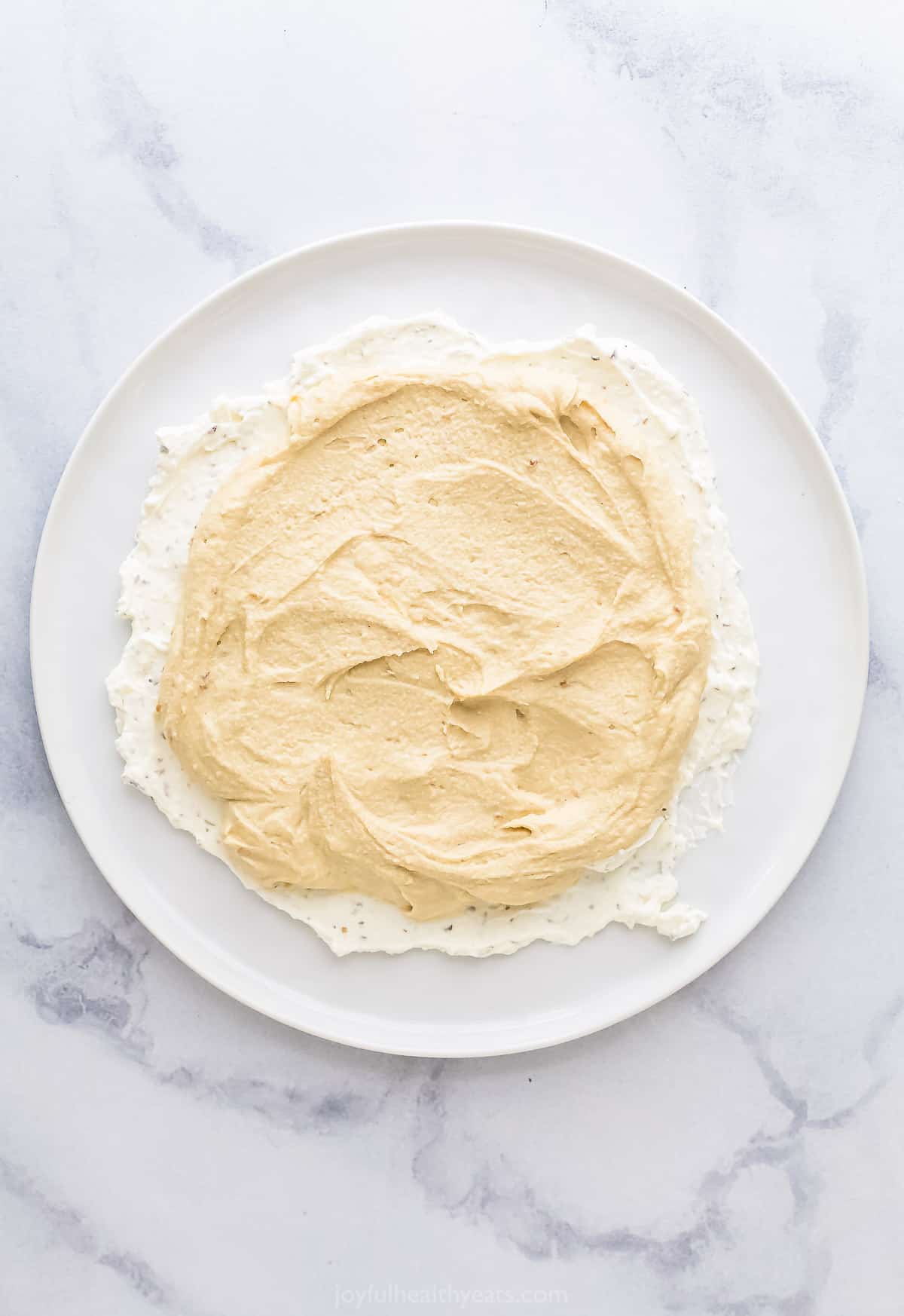 A large plate containing a layer of whipped feta topped with a layer of original hummus