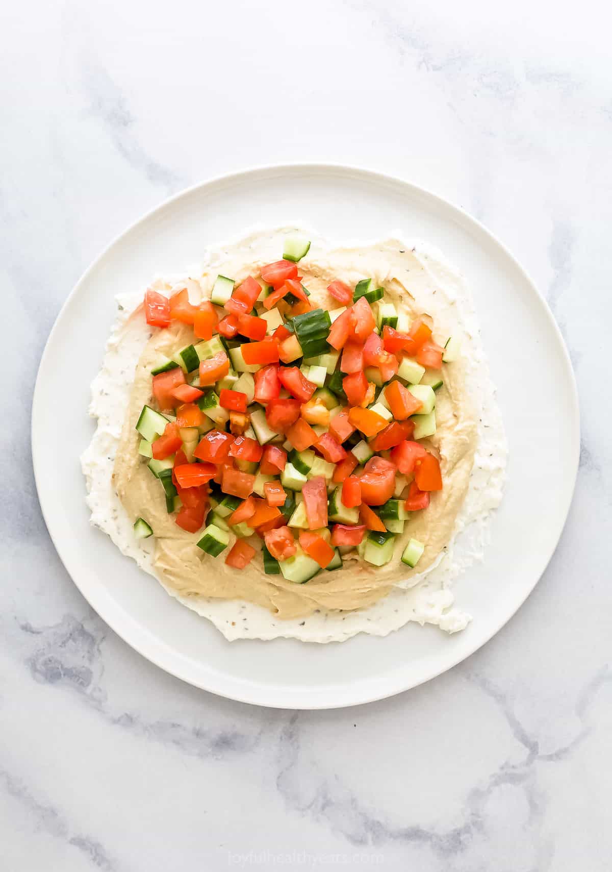 Chopped tomatoes layered on top of the diced cucumbers, hummus and whipped feta