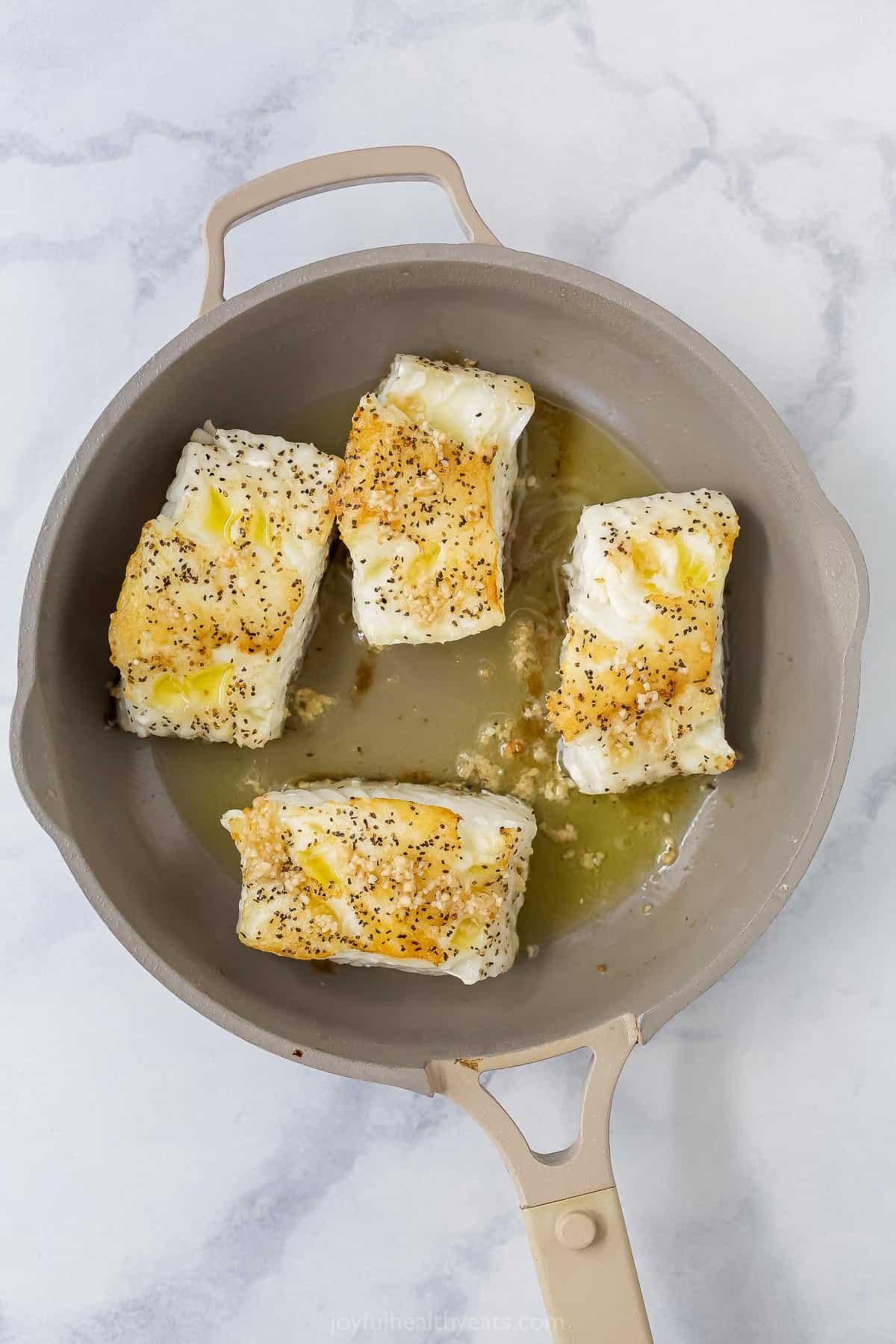 seasoned sea bass in a pan with ghee and garlic