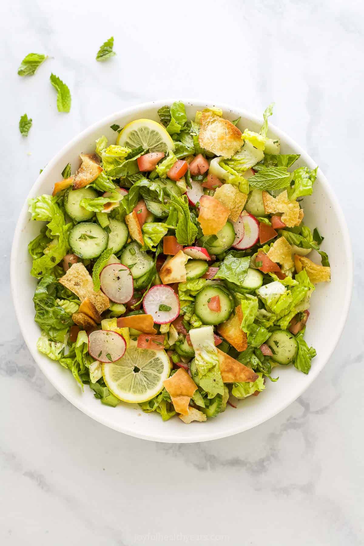 A bowl of fattoush salad on a marble kitchen countertop