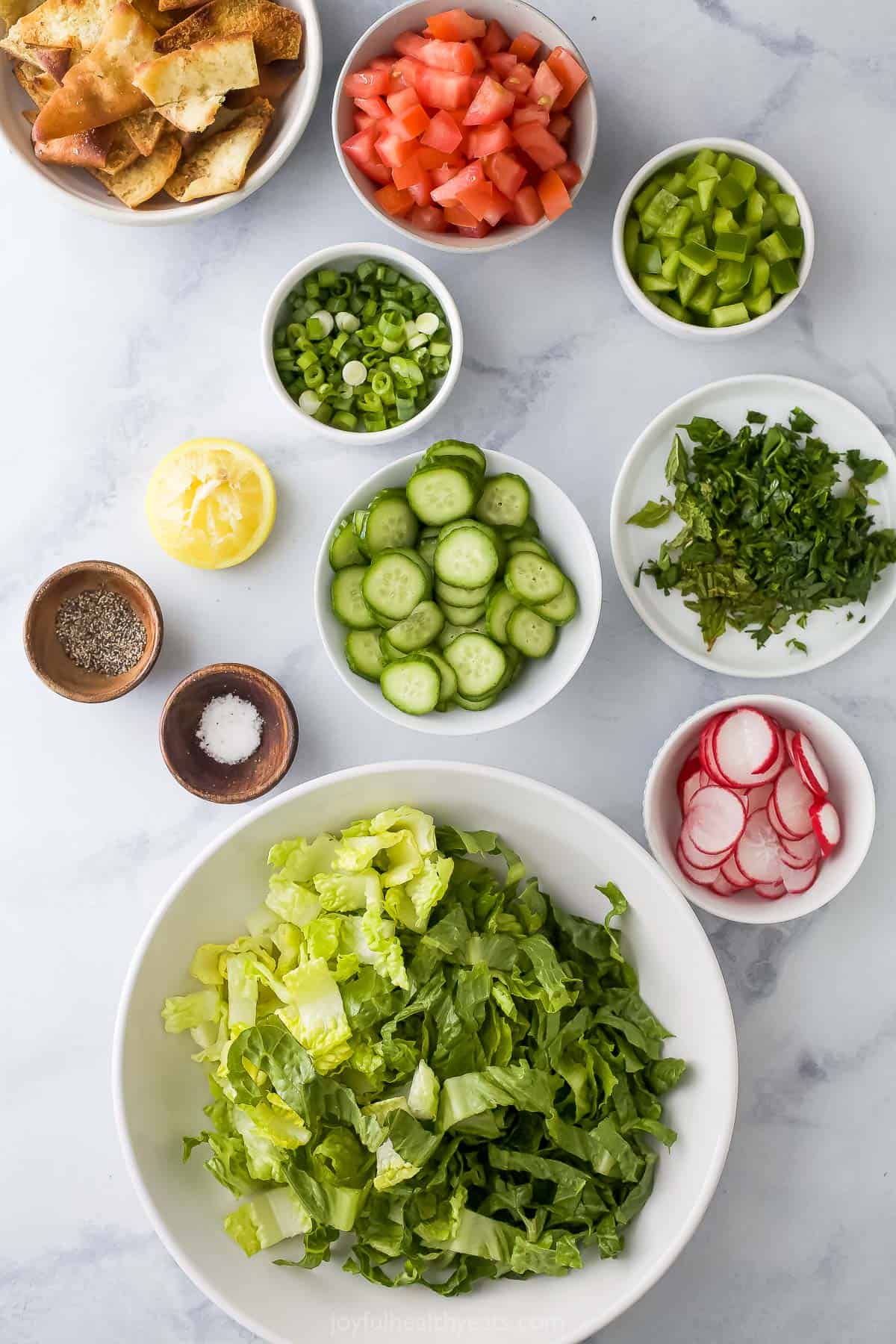 Lettuce, radishes, salt, pepper and the rest of the ingredients laid out on a marble surface