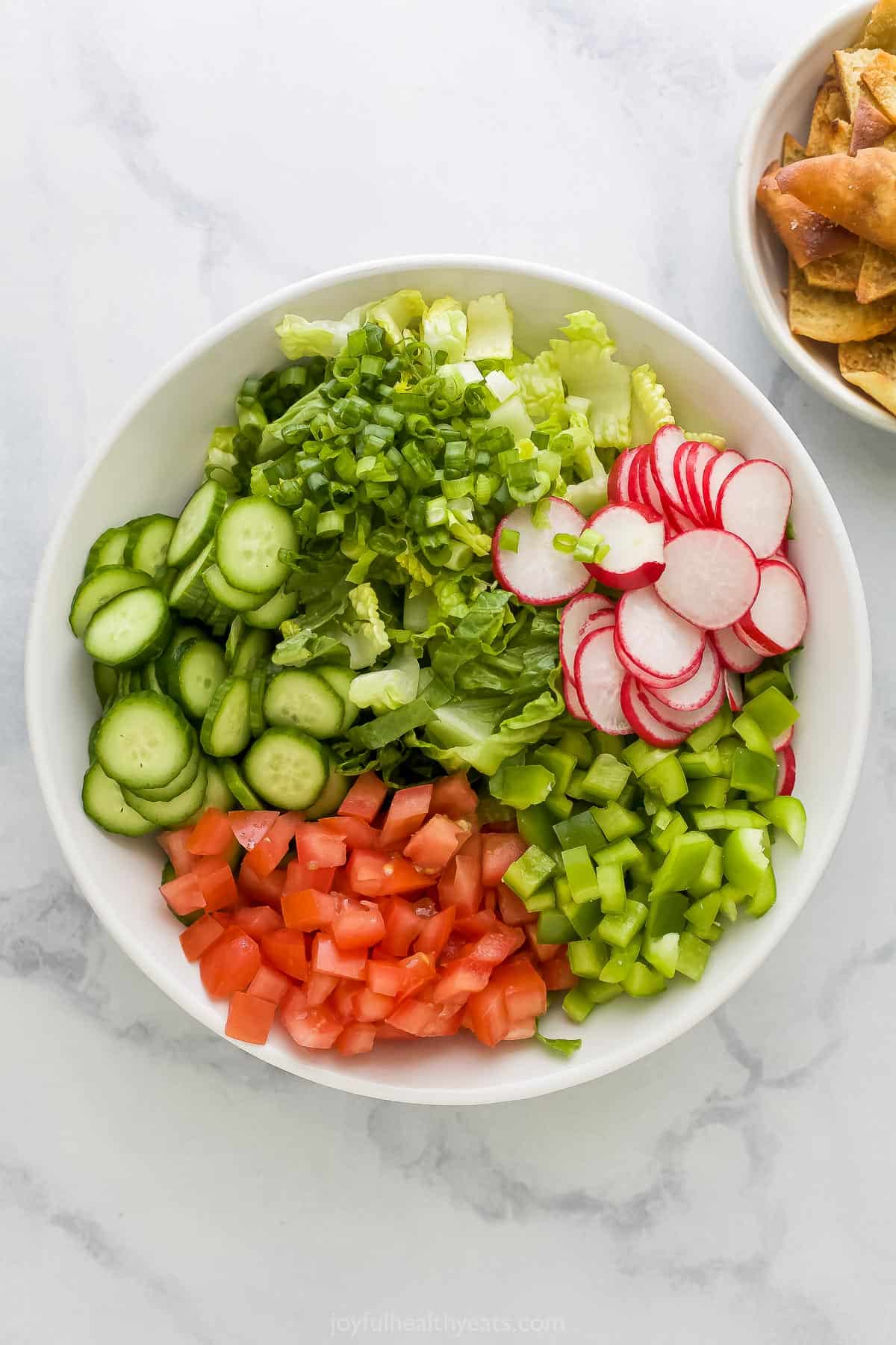 All of the prepared salad veggies in a white mixing bowl