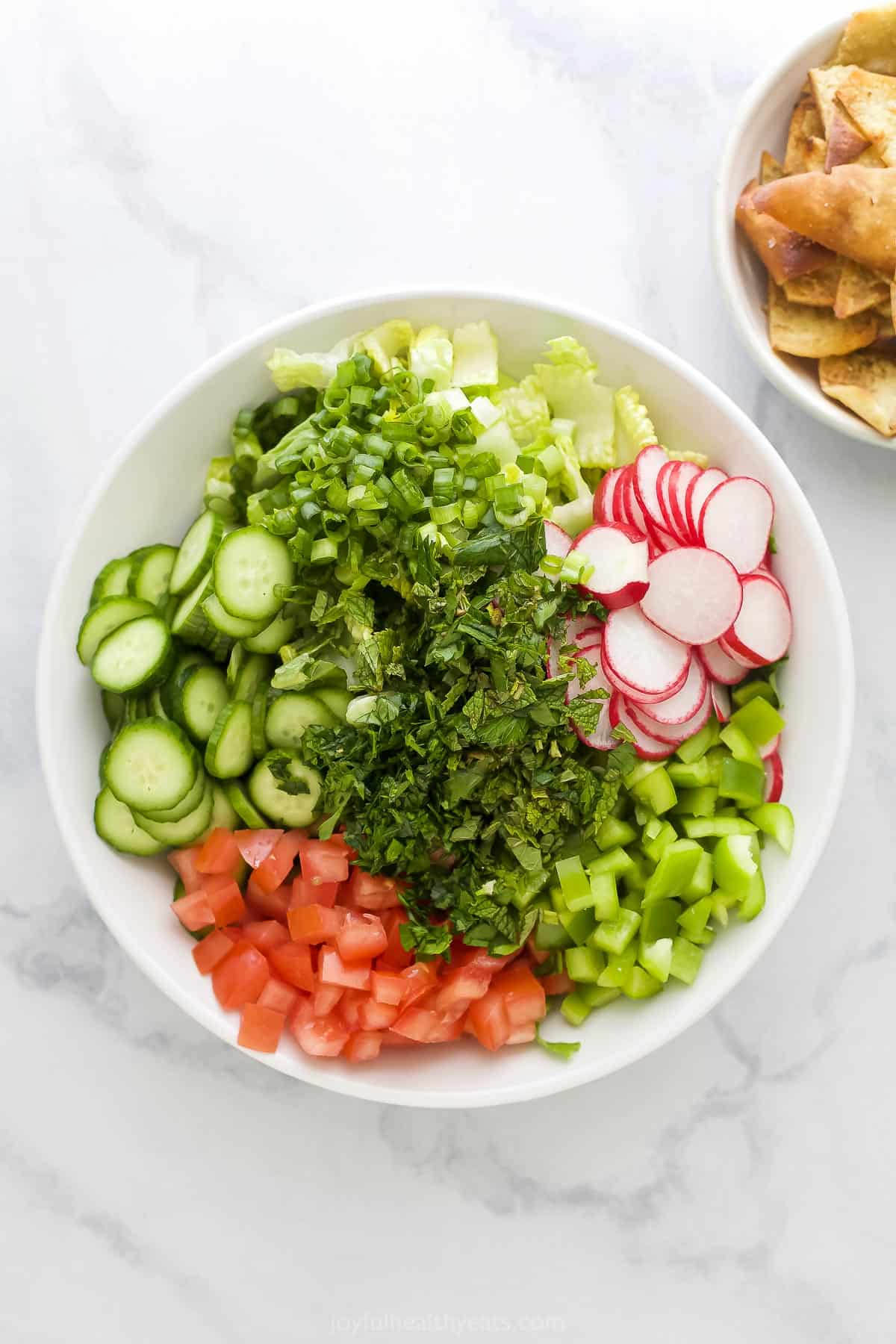 Chopped lettuce, tomato, mint, parsley, radishes, green pepper, onion and cucumber in a large mixing bowl