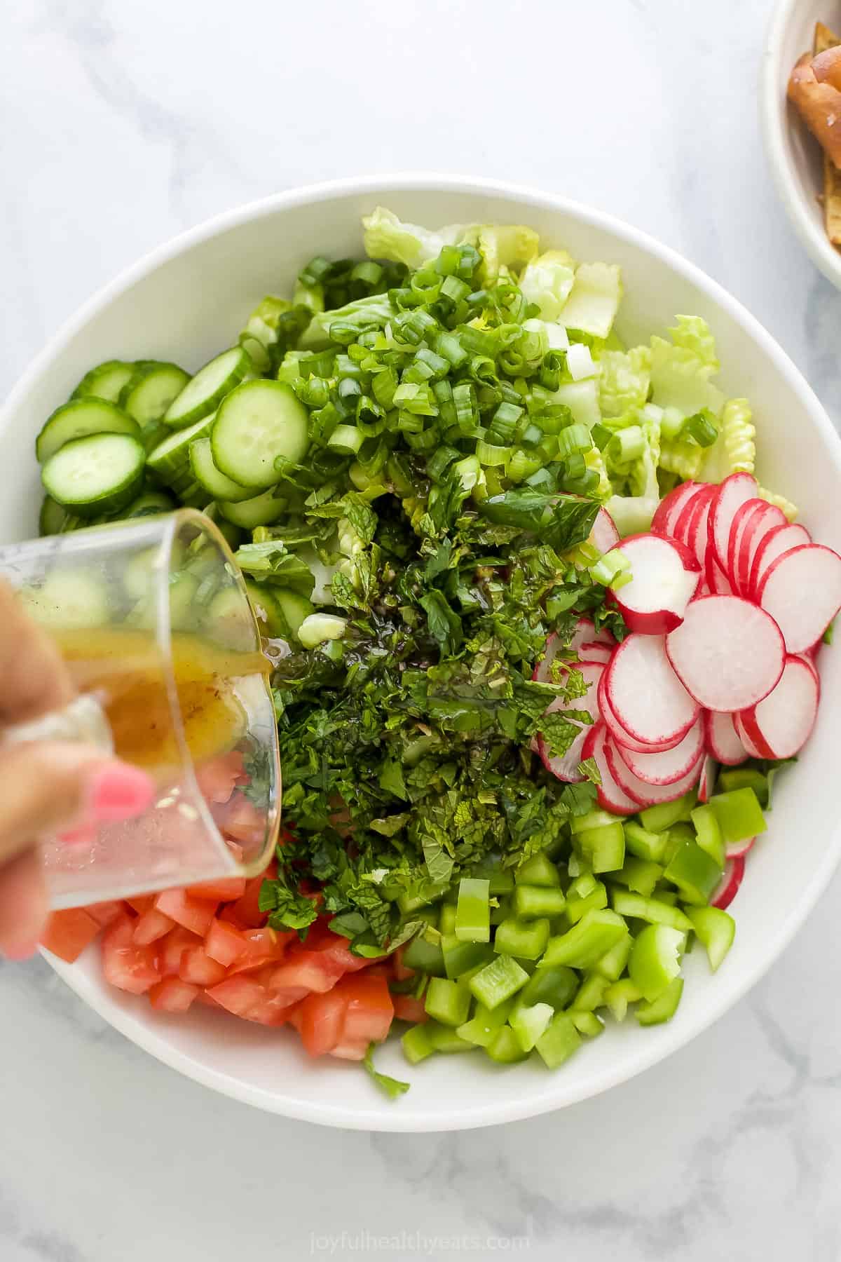 Sumac vinaigrette being poured over a bowl of chopped veggies and herbs