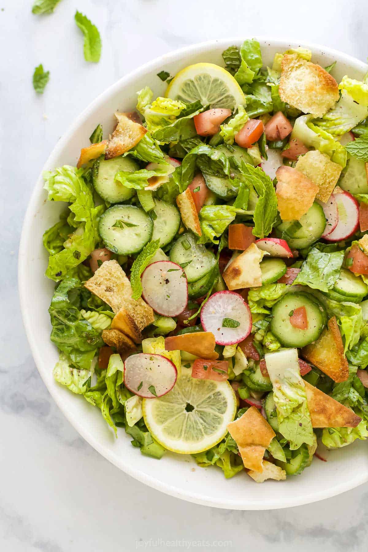 A close-up shot of fattoush salad inside of a large white serving bowl