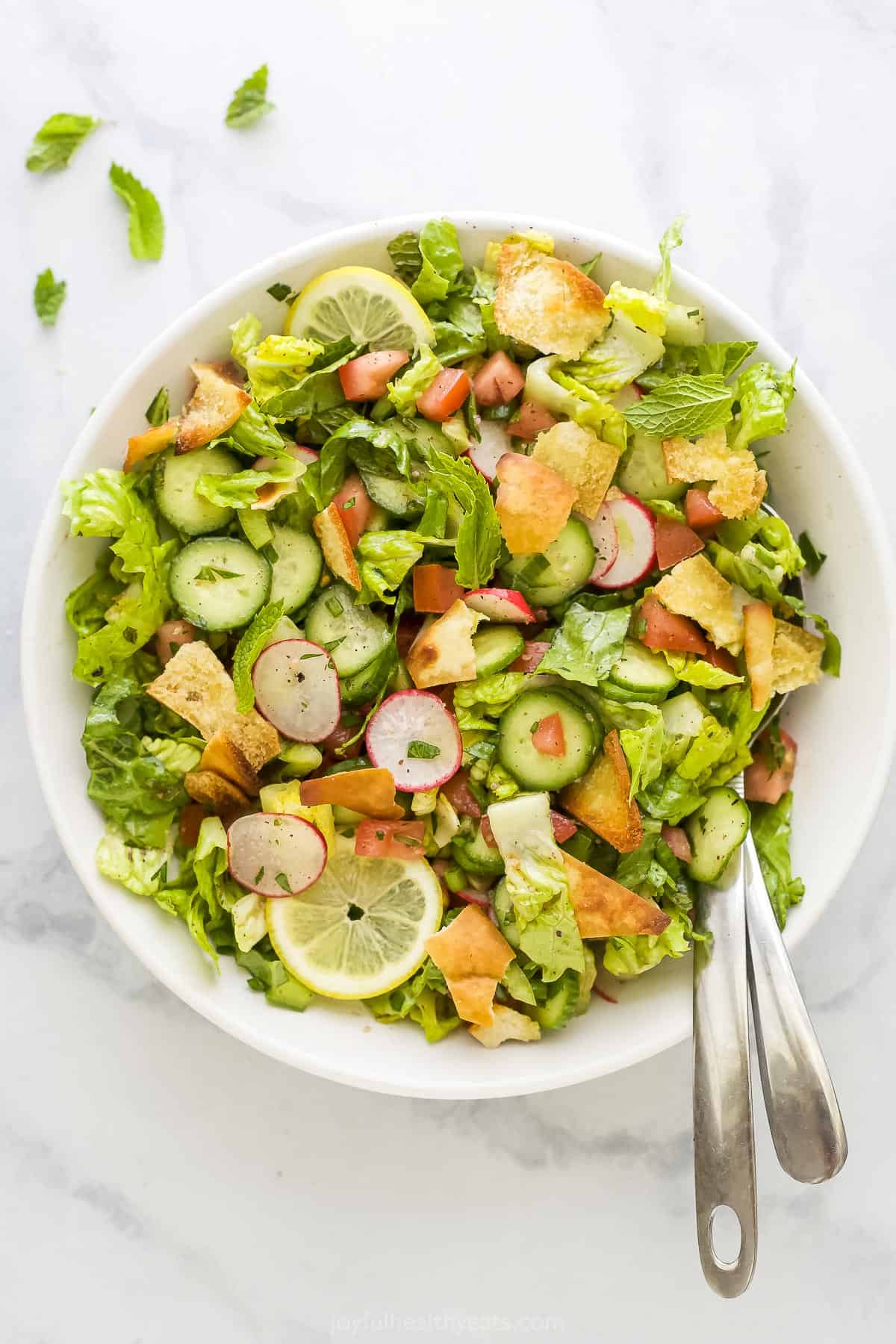 A large bowl of fattoush salad with two metal spoons inside