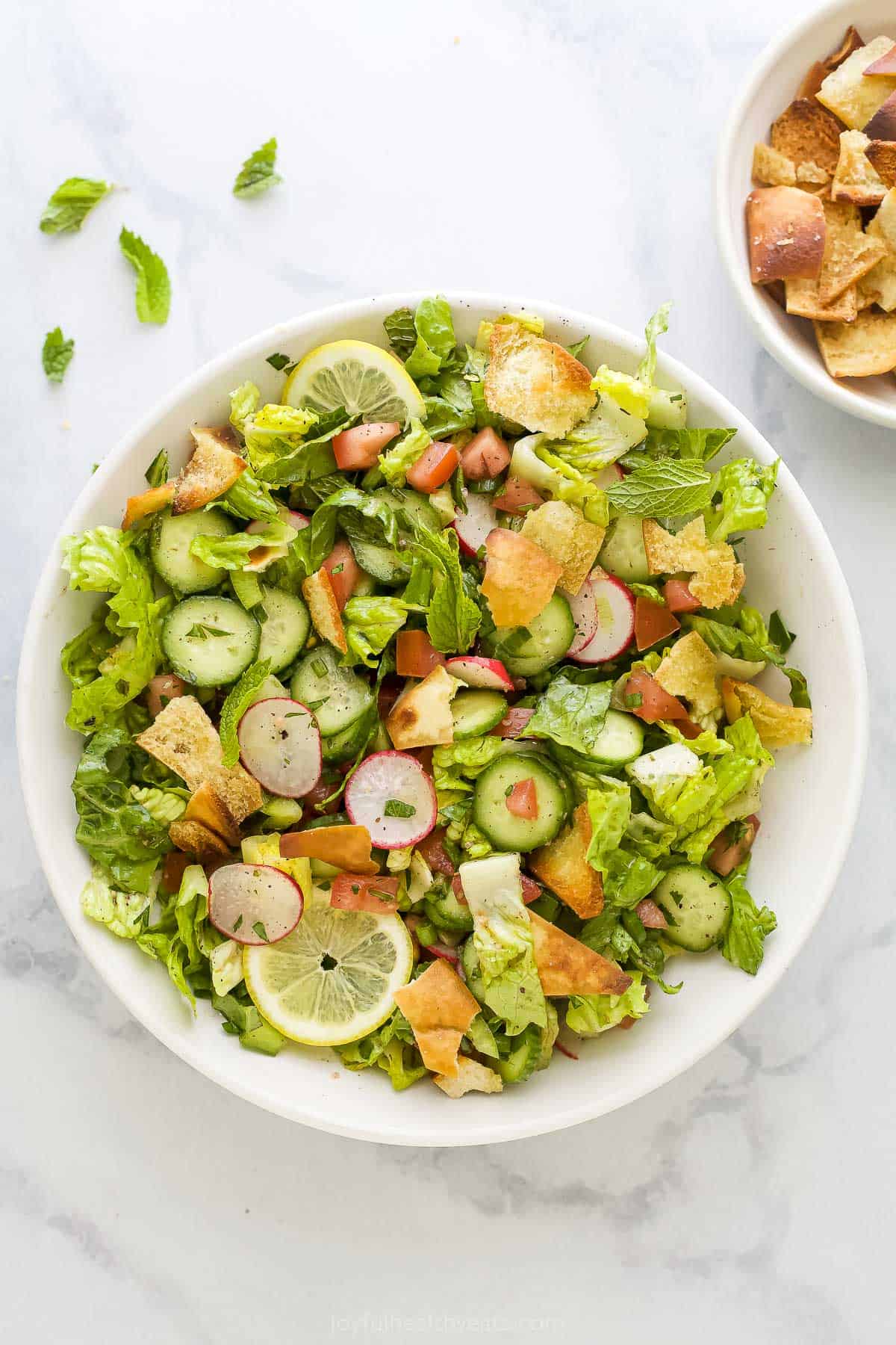 A bowl of Lebanese salad beside a dish full of pita croutons